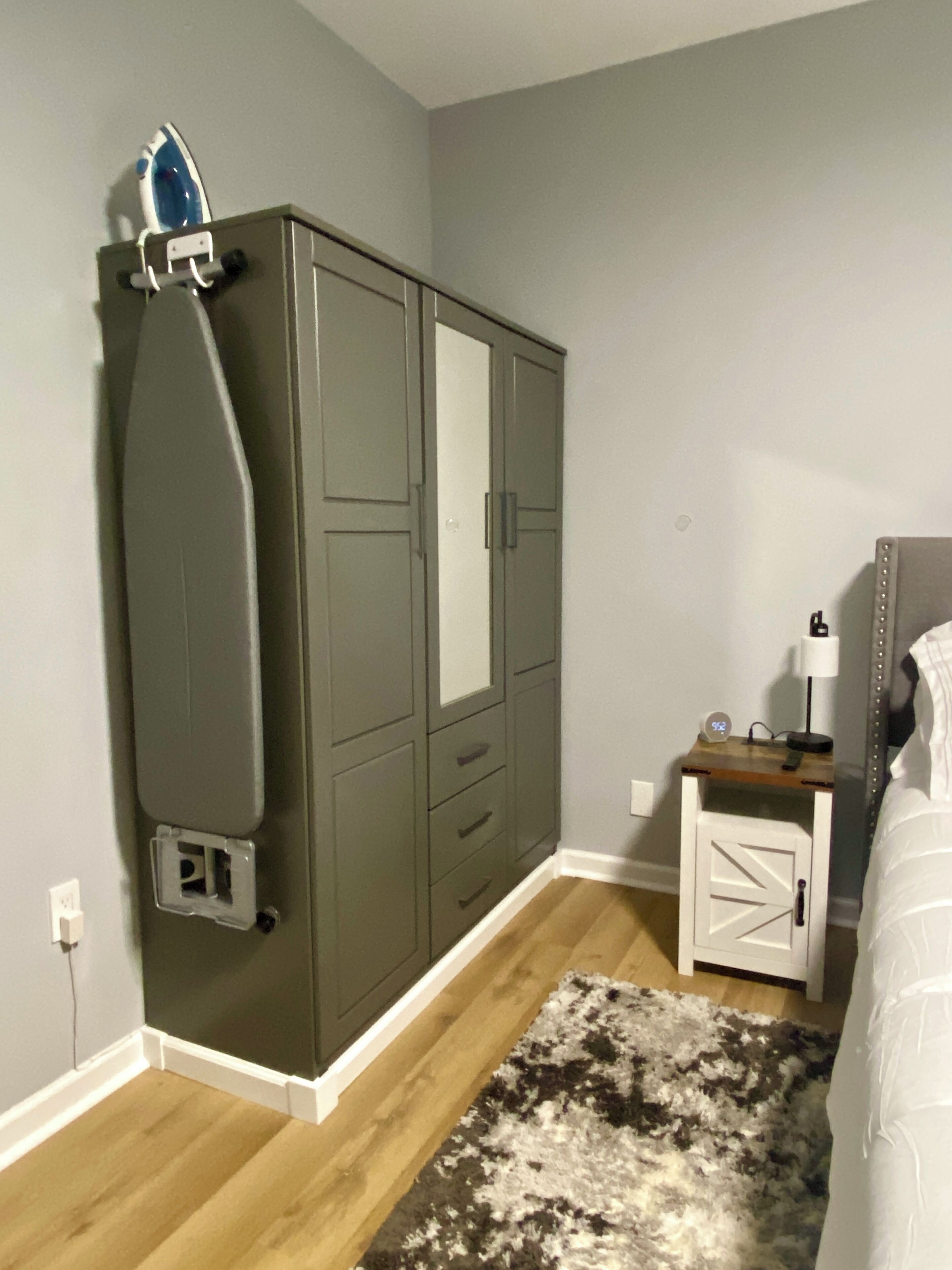 A bedroom with a wardrobe, bedside table, and a rug.