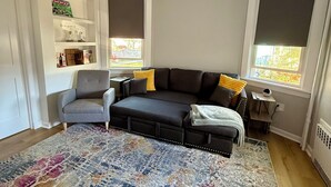 A modern living room with a grey sofa, a patterned rug, and a small side table. - Charming suite with patio, heating, WiFi, free parking in welcoming New Rochelle (New Rochelle)