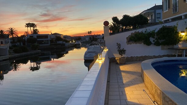A marina with a boat docked, a swimming pool, and a sunset view. - Pleasant house on the canal with pool (Castelló d'Empúries)