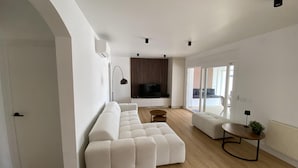 A modern living room with a sectional sofa, a small round table, and a TV mounted on the wall. - Pleasant house on the canal with pool (Castelló d'Empúries)