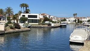 A marina with boats docked, a modern white building, and palm trees. - Pleasant house on the canal with pool (Castelló d'Empúries)