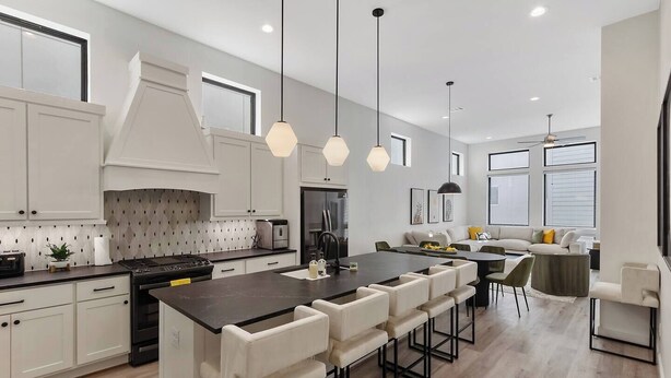 Une cuisine moderne avec des meubles blancs, un îlot central doté de tabourets de bar, un éclairage suspendu et un coin repas comprenant un canapé et des chaises.