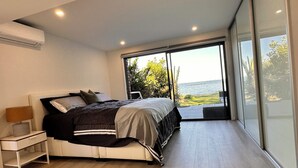Une chambre à coucher moderne, dotée d’un grand lit, d’une table de chevet et offrant une vue sur la mer grâce à de grandes fenêtres.