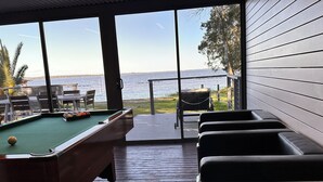 Une table de billard avec des billes, une queue de billard et une vue sur la mer par de grandes fenêtres.
