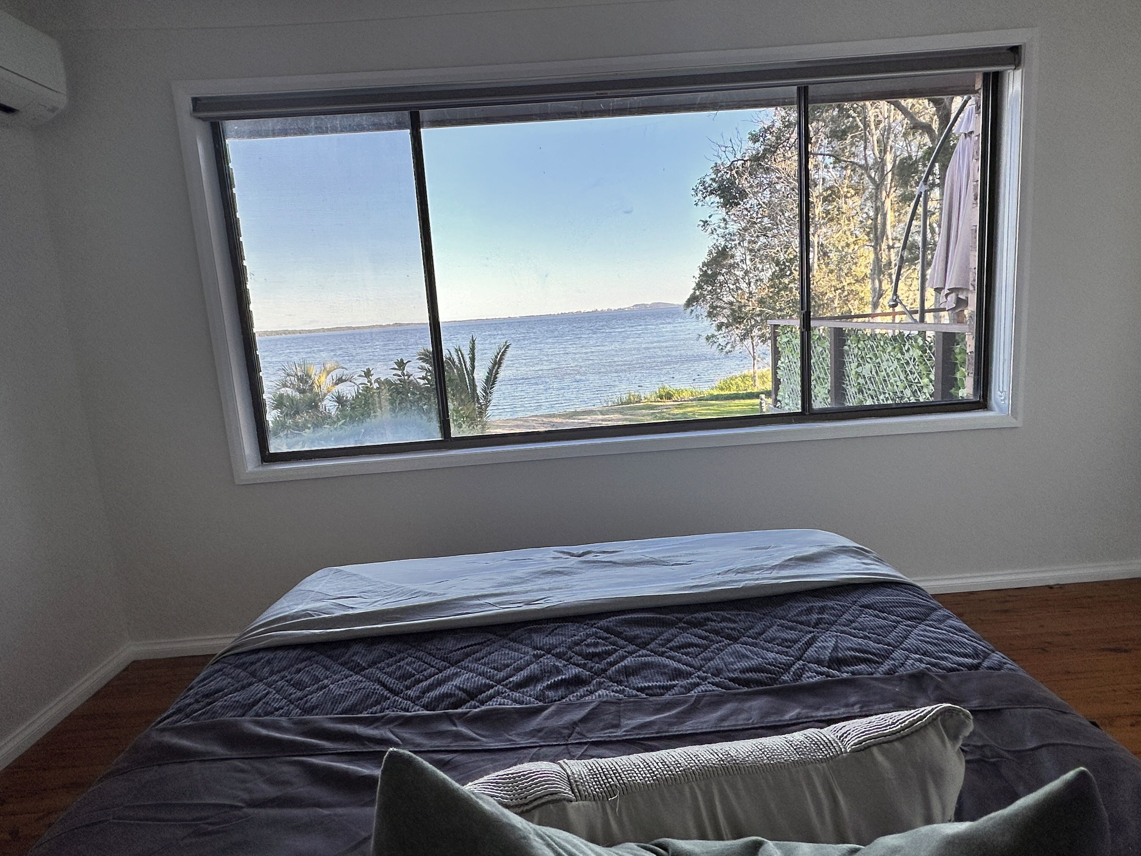 Ein Zimmer mit großem Fenster und Blick auf ein Gewässer und viel Grün.