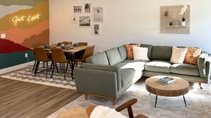A modern living room with a sectional sofa, a dining table with chairs, and a coffee table. There are wall art pieces and a neon sign on the wall. - Alpine Townhouse - stylish, peaceful, and walking distance to Ellicottville (Ellicottville)