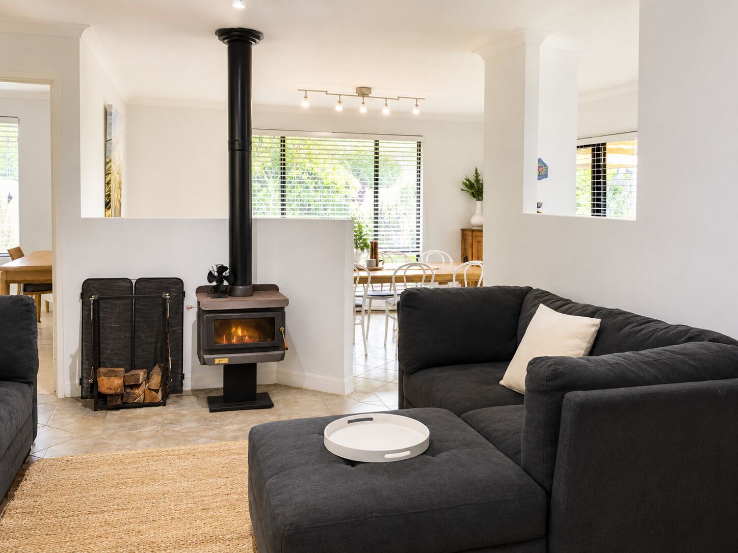 Uma sala de estar moderna com lareira a lenha, sofá, área de jantar e uma janela grande.