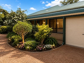 A building with a green roof, a gravel driveway, and a landscaped garden with various plants and trees.