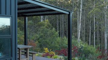 A wooden deck with a table and bench, surrounded by a garden with various plants and trees in the background.