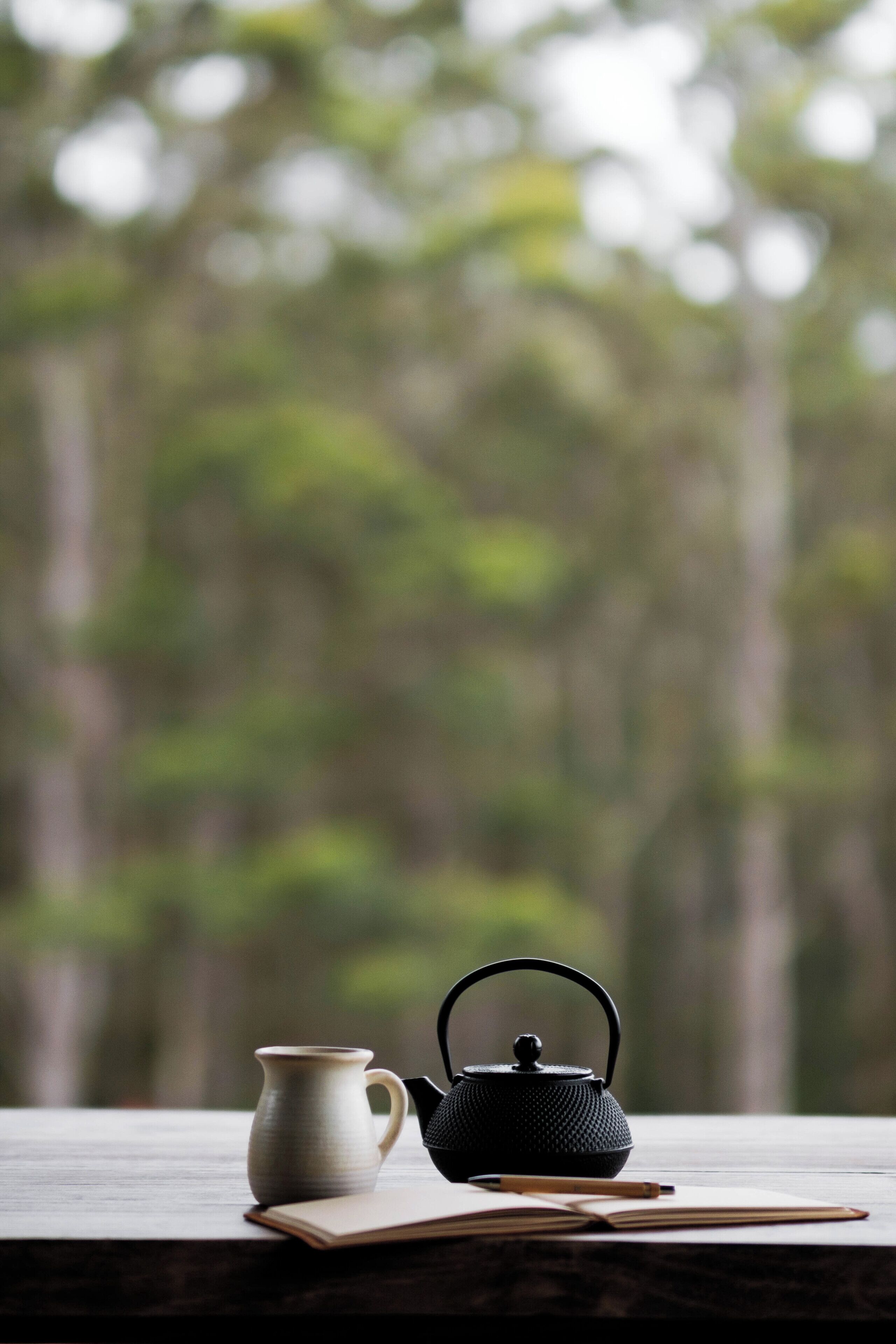 A wooden table with a black teapot, a white pitcher, and a book.