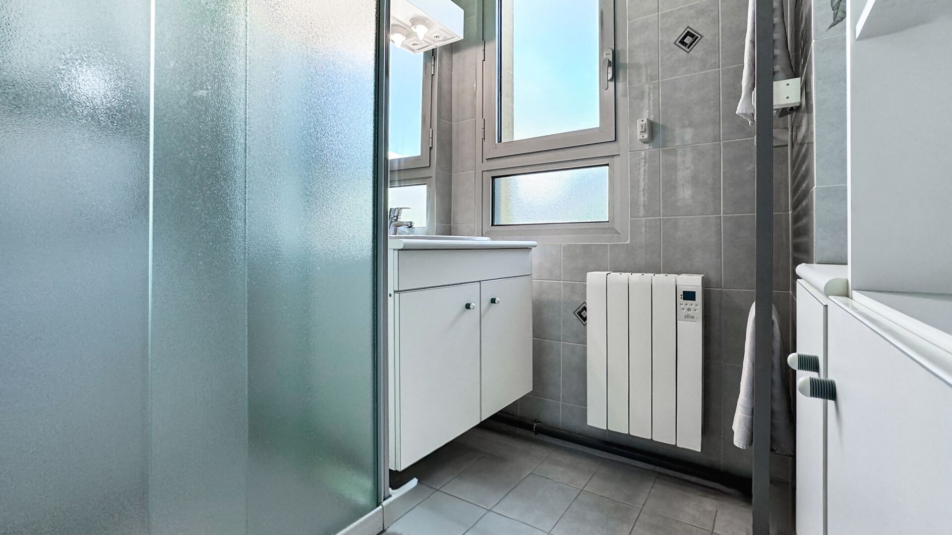 Un baño moderno con cabina de ducha de vidrio, lavamanos blanco y calefacción integrada.