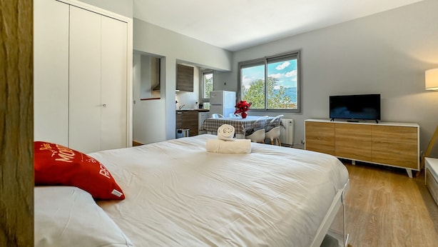 A hotel room with a bed, a TV, a wooden dresser, a kitchenette, and a window with a view. - Sujadaro Refuge (Osséja)