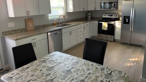 Eine moderne Küche mit weißen Schränken, einer Granit Arbeitsplatte, Edelstahlgeräten und einem Essbereich mit Tisch für zwei Personen.
