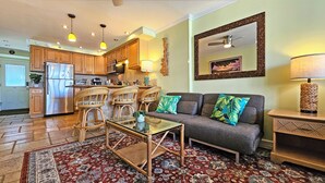 Una sala de estar con sofá, mesa de centro y sillas, una cocina con muebles de madera y electrodomésticos, y un comedor con mesa y sillas.
