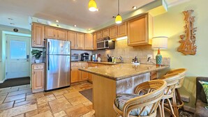 Una cocina con armarios de madera, electrodomésticos de acero inoxidable, una isla central con sillas y un elemento decorativo en la pared.