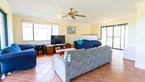 A living room with a television, two sofas, a ceiling fan, and large windows. - Meelup Ridge (Dunsborough)