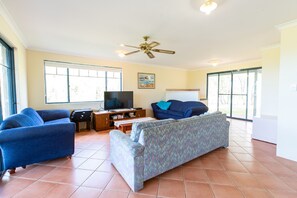 A living room with a television, two sofas, a ceiling fan, and large windows. - Meelup Ridge (Dunsborough)