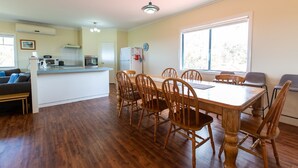 A spacious kitchen with a dining area, wooden chairs, and a large window providing natural light. - Meelup Ridge (Dunsborough)