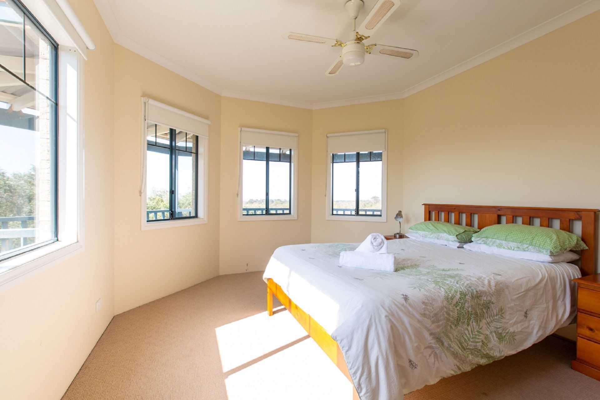 Une chambre à coucher avec un lit, un ventilateur de plafond et trois fenêtres.