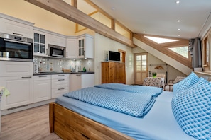 A bedroom with a bed, a wooden ceiling, and a kitchen area with cabinets and appliances.