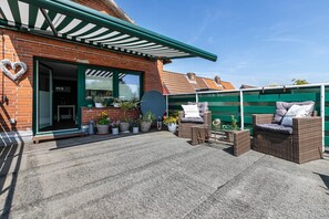 Une terrasse avec des meubles en osier, des plantes en pot et une décoration en forme de cœur sur un bâtiment en briques.