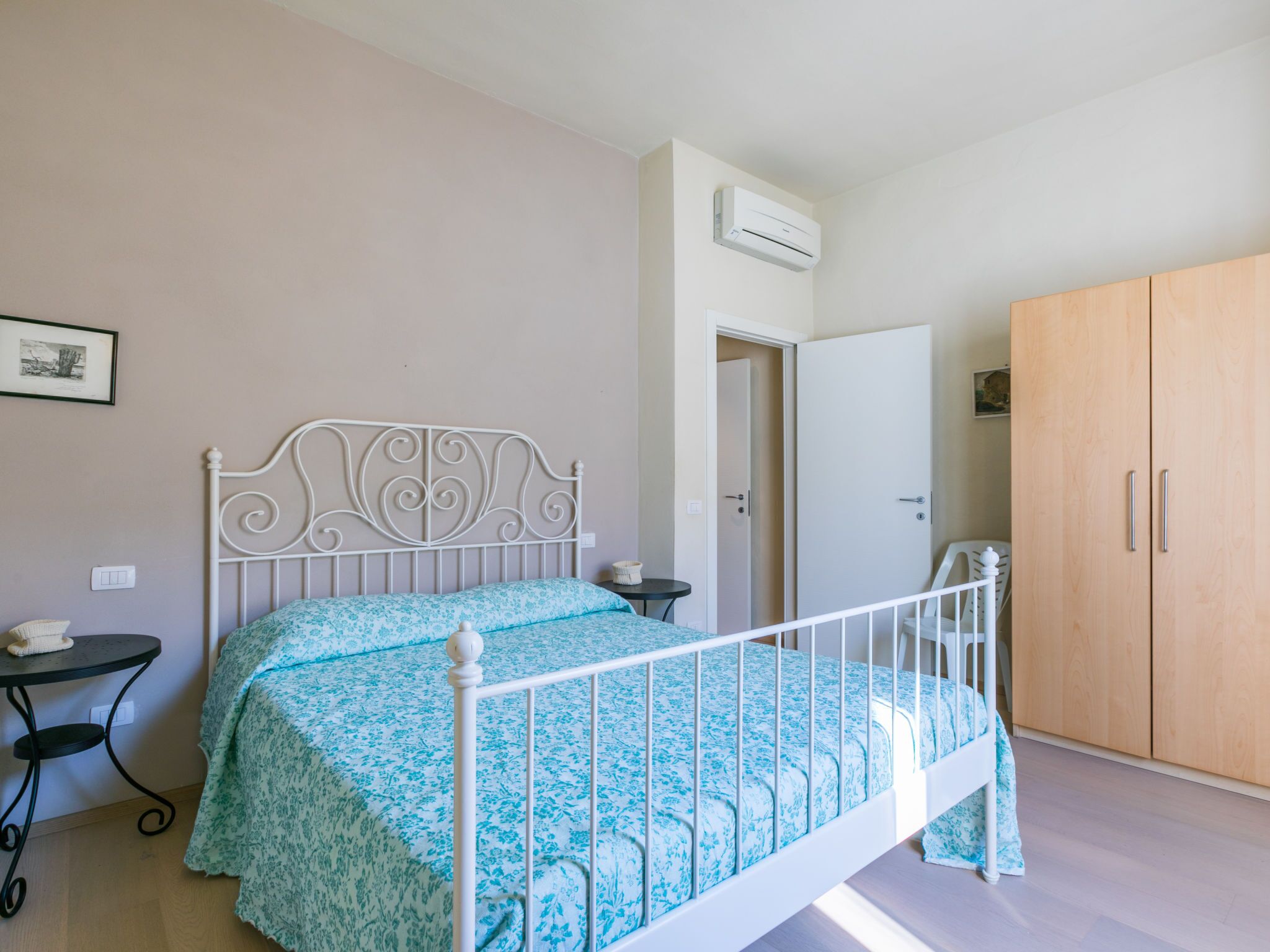 A bedroom with a bed, a wardrobe, a small table, and an air conditioning unit.