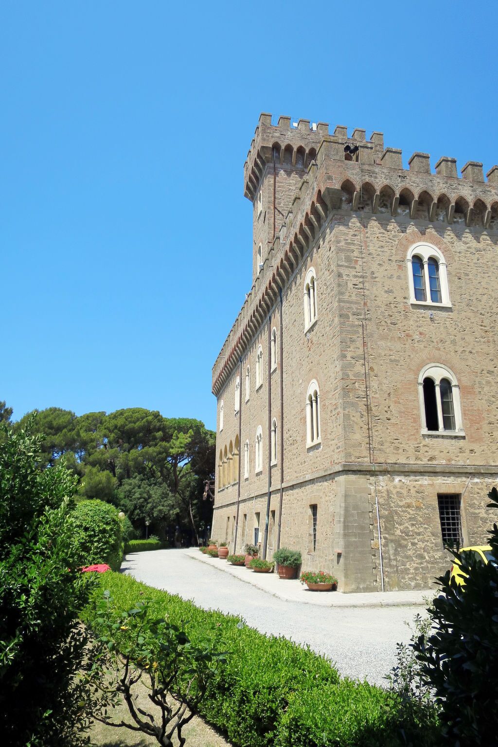Un edificio storico in pietra con finestre ad arco e una torre merlata, circondato da verde curato.