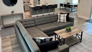 Un salon moderne avec un canapé d’angle, une table basse et un coin repas, la cuisine étant visible au fond.