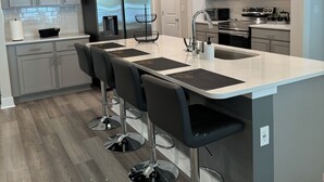 Une cuisine moderne avec des meubles gris, des appareils en acier inoxydable et un îlot central doté de tabourets de bar.