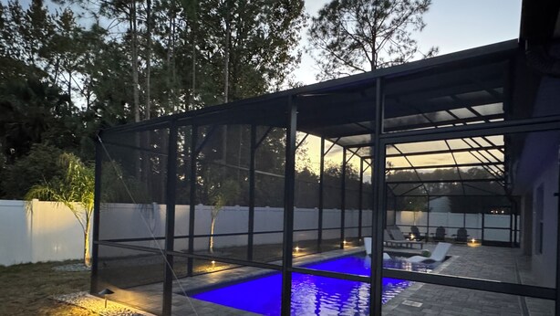 Un espace piscine extérieur moderne, doté d’une structure en verre, d’un revêtement de sol en pierre et d’une terrasse avec des sièges.