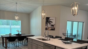 Une cuisine moderne dotée d’un grand îlot central, d’appareils électroménagers en acier inoxydable et de luminaires suspendus.