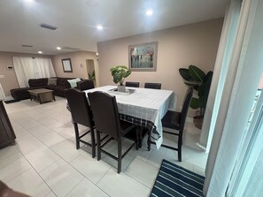 A dining area with a table set for four, surrounded by chairs, in a room with a sofa and a large plant. - Charming 3-bedroom house with pool, AC, WiFi in pleasant Tampa (Tampa)