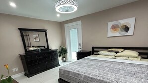 Quarto com uma cama grande, cômoda, espelho e luminária no teto.