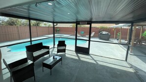 Uma área de varanda coberta com piscina, móveis de exterior e vista para o quintal.