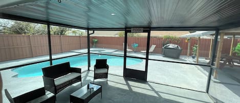 A covered patio area with a pool, outdoor furniture, and a view of the backyard.