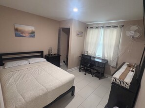 Ein Schlafzimmer mit Bett, Schreibtisch und Ventilator.