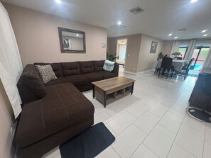 A living room with a brown sectional sofa, a wooden coffee table, and a dining area with a table and chairs.