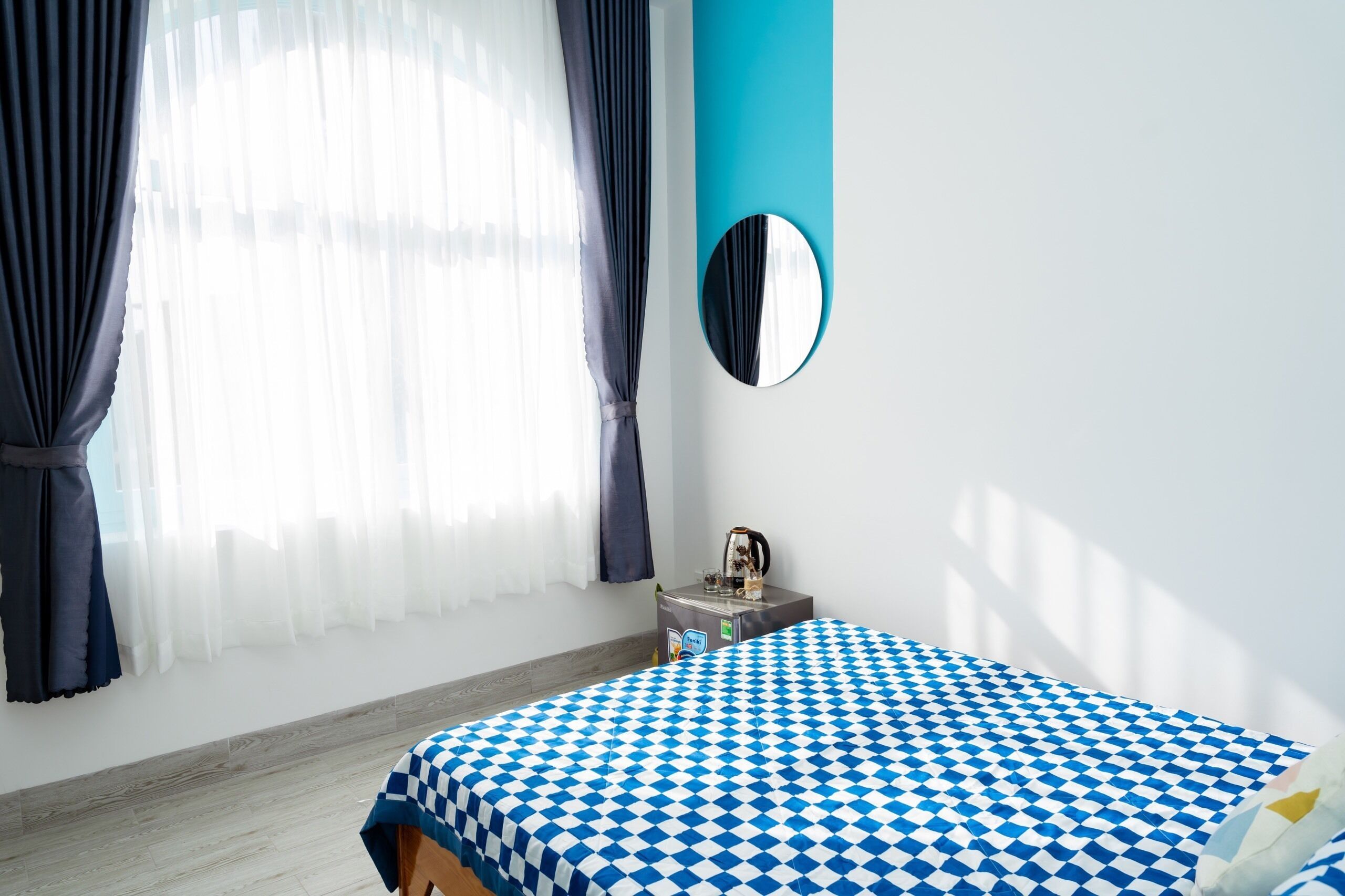 Ein Schlafzimmer mit kariertem Bettbezug, einem Nachttisch mit Wasserkocher und einem Spiegel an der Wand.