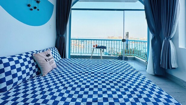 A hotel room with a checkered bedspread, a view of the sea through a balcony, and a blue wall decoration. - Xing Ocean Homestay VT by Bay Luxury (Ho Chi Minh City)
