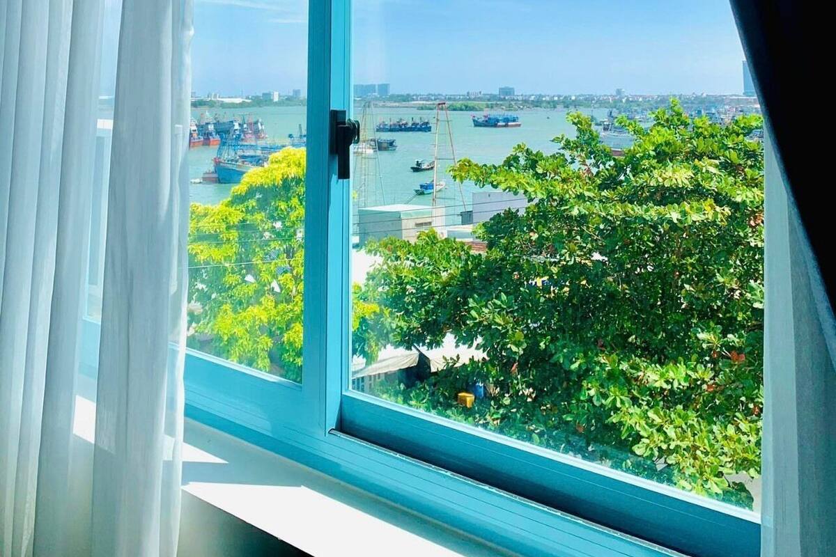 Une fenêtre donnant sur un port, des bateaux et de la verdure.