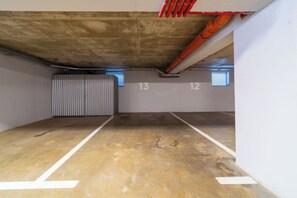 Un parking souterrain vide, avec des planchers et des murs en béton, des places de stationnement numérotées et une porte en métal.