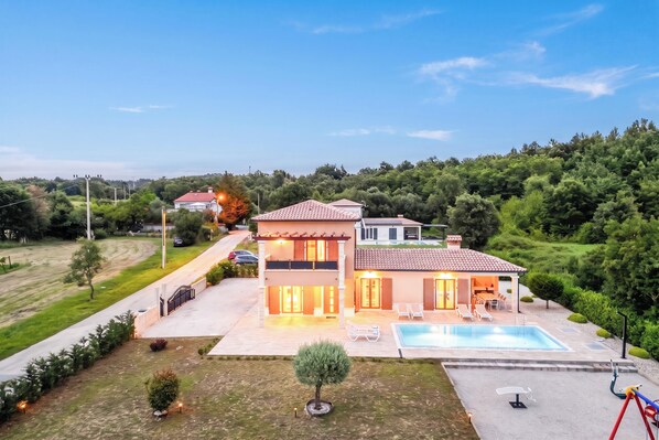 A two-story house with a swimming pool, a covered patio, and a well-maintained garden.