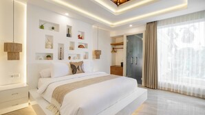 A modern bedroom with a large bed, built-in shelving with decorative items, a walk-in closet, and a large window with curtains. - Villa Dove By OriVista (Canggu)