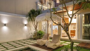 A pool area with lounge chairs, a small tree, and a dining area visible through glass doors. - Villa Dove By OriVista (Canggu)