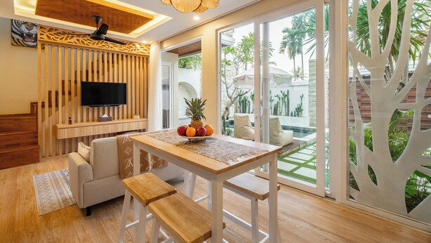 A modern living room with a wooden dining table, a sofa, and a TV mounted on a wooden panel. - Villa Dove By OriVista (Canggu)