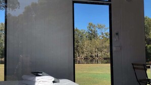 Un dormitorio con una cama grande, una silla y vistas a árboles y un cuerpo de agua.