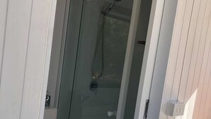 Ducha envuelta en vidrio con cabezal de ducha manual, puerta con manija y piso de madera.