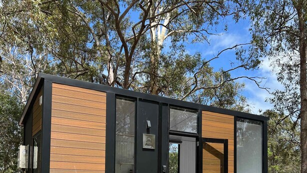 Una cabaña moderna y compacta, con fachada de madera, ventanas grandes y una terraza.