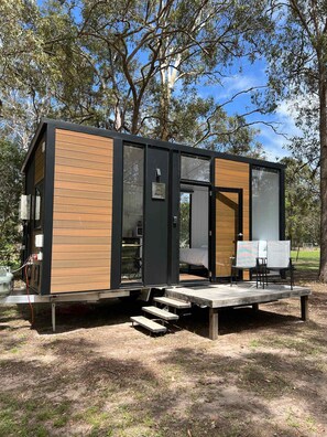 A modern, compact cabin with a wooden exterior, large windows, and a deck area. - Sandy Strait Shack by Tiny Away (Booral)