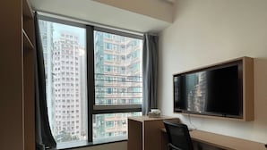 A hotel room with a bed, a desk, a chair, a TV, and a large window with a view of high-rise buildings. - China Rich Oriental Hotel (Hong Kong)